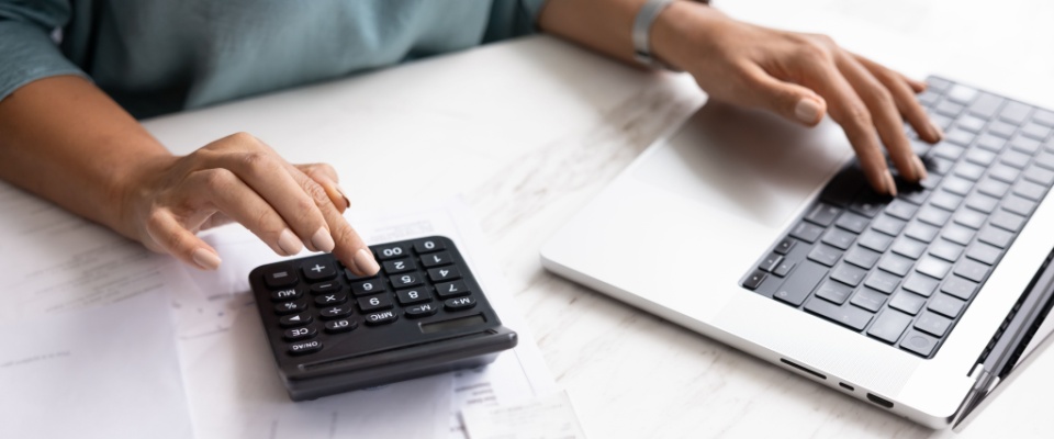 Person using a calculator and laptop to review expenses, analyzing premiums and deductibles to compare renters insurance costs.