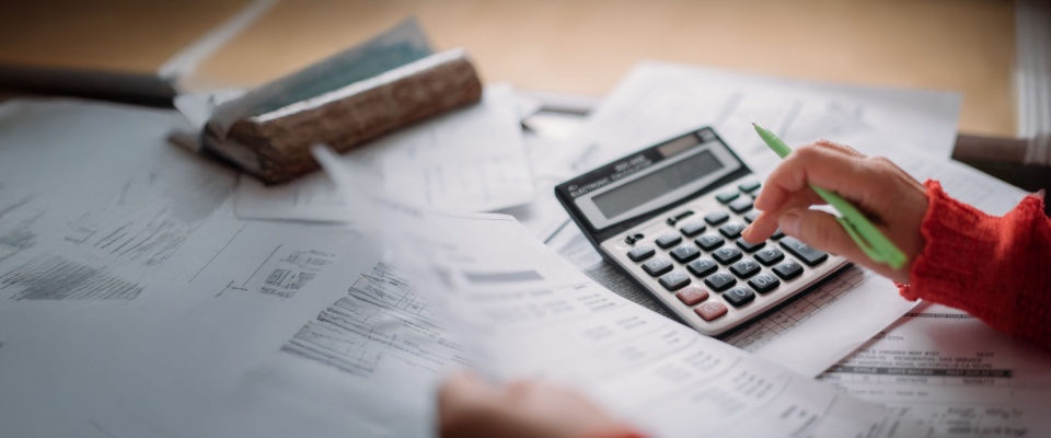 Hand using a calculator over utility bills and paperwork, analyzing monthly expenses and changes in Texas electricity rates.