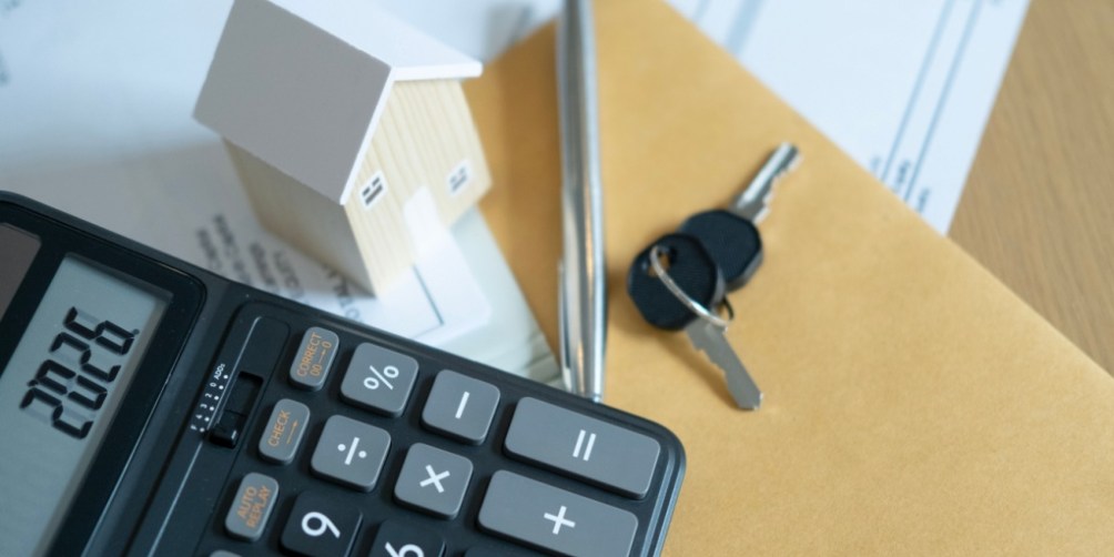 Calculator, house model, and keys on paperwork, representing financial planning decisions about how much of income should go to rent.