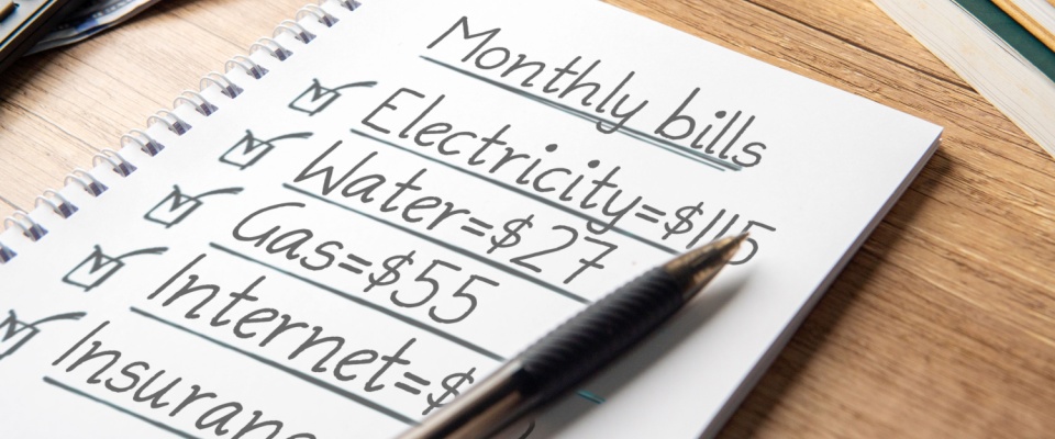 Notebook listing monthly bills like electricity, water, and gas, helping renters evaluate how much of income should go to rent within a realistic budget.