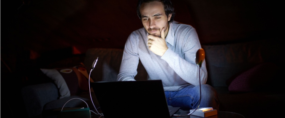 Man working on a laptop by dim light during a rolling blackout, illustrating how temporary outages can disrupt daily routines.