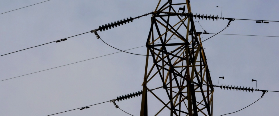 High-voltage power transmission tower against a dark sky, representing grid strain and infrastructure issues that can cause a rolling blackout.
