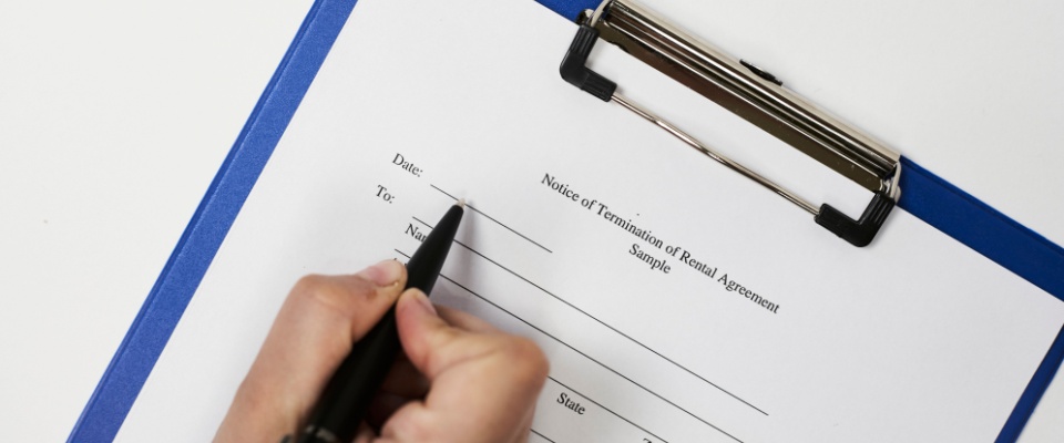 Close-up of a hand holding a pen over a Notice of Termination of Rental Agreement form on a blue clipboard, illustrating the flexible lease-ending process common with month-to-month rentals.