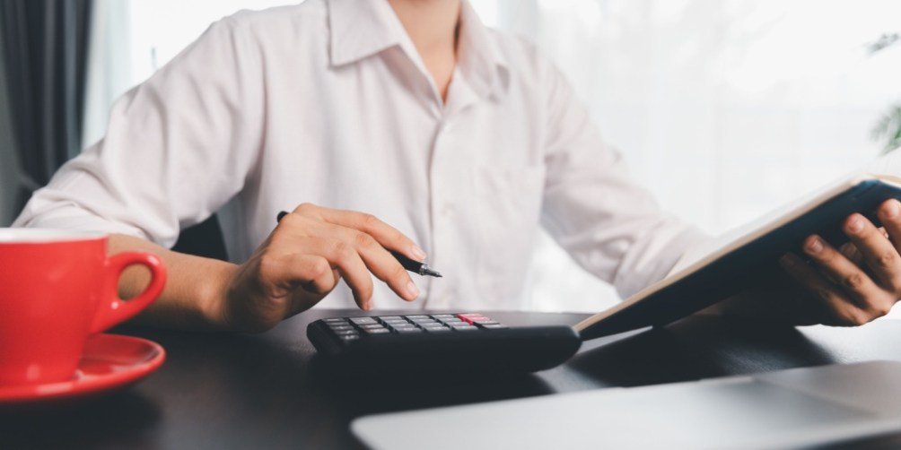 Individual calculating expenses at a desk with calculator and documents while evaluating whether renters insurance is tax deductible on a federal tax return.