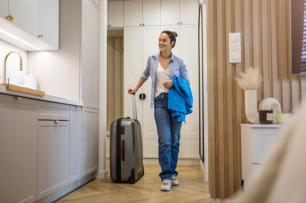 Smiling woman with a suitcase walking into a modern apartment, representing the easy move-in experience that month-to-month rentals offer tenants.